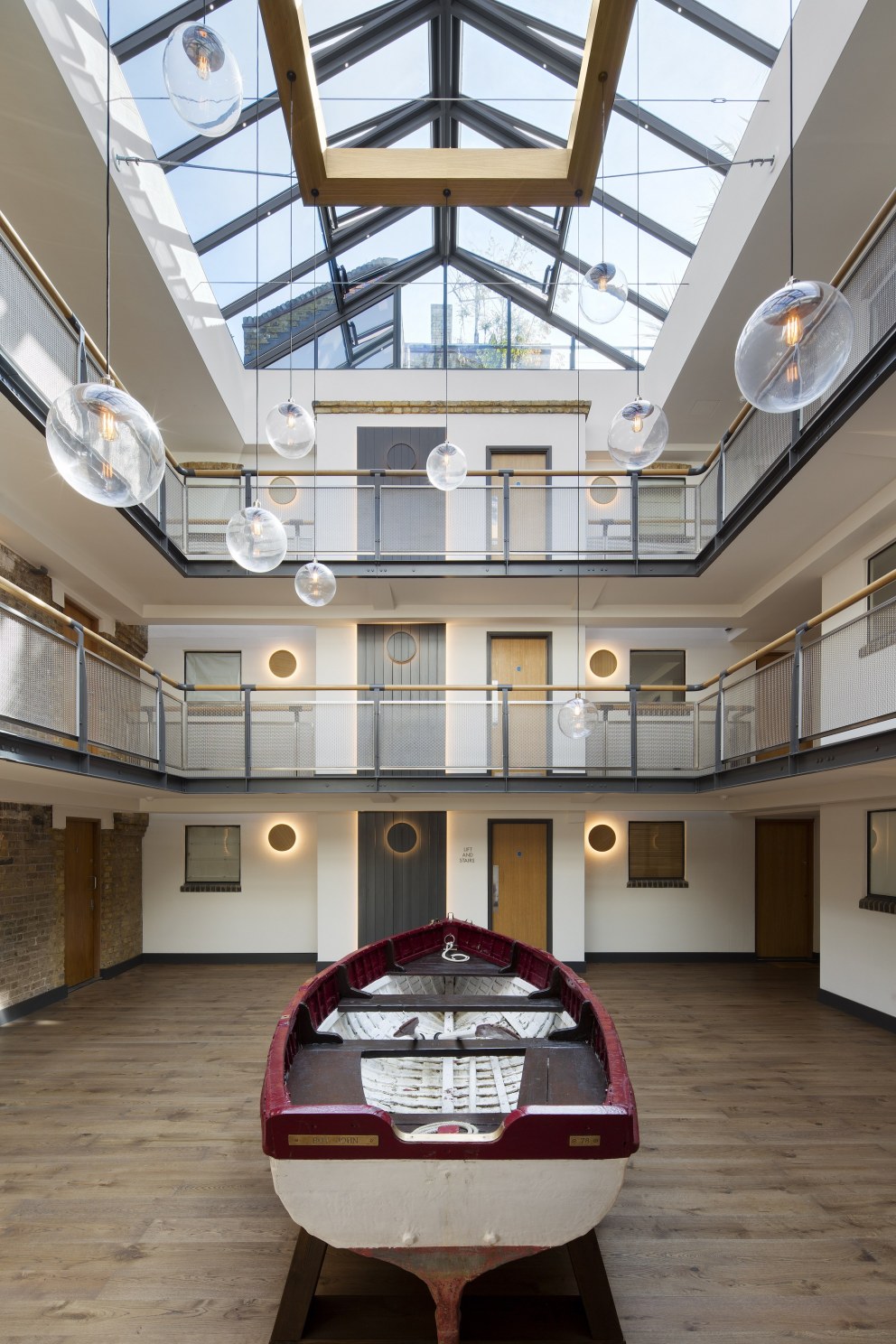 Residential apartment building atrium - Wapping High Street | Main atrium with bespoke industrial chandelier and restored lifeboat | Interior Designers